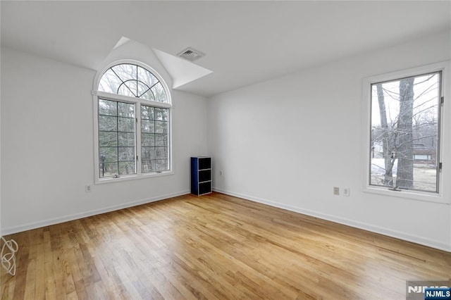 unfurnished room featuring lofted ceiling, hardwood / wood-style floors, visible vents, and baseboards