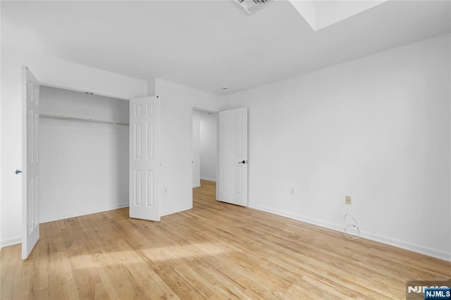 unfurnished bedroom with a closet, wood finished floors, visible vents, and baseboards