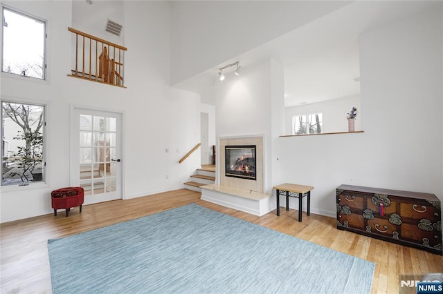 interior space featuring a glass covered fireplace, visible vents, a towering ceiling, and wood finished floors