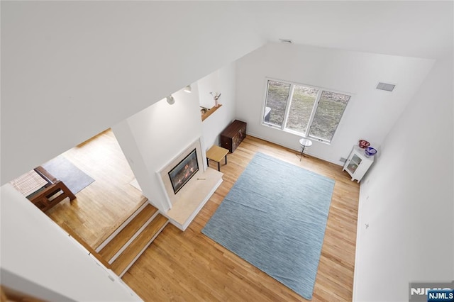 living room with vaulted ceiling, wood finished floors, a glass covered fireplace, and visible vents