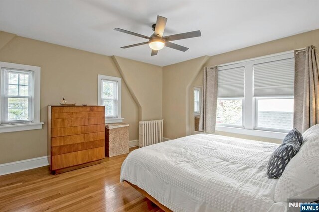 bedroom featuring radiator, multiple windows, baseboards, and light wood-type flooring