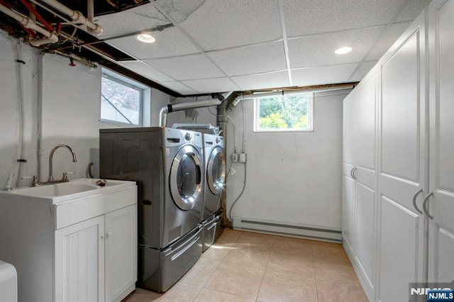 laundry room with a healthy amount of sunlight, light tile patterned flooring, baseboard heating, washing machine and clothes dryer, and cabinet space