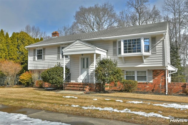 split foyer home with a chimney, a front lawn, and brick siding