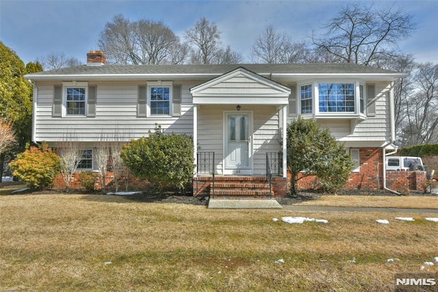 bi-level home featuring brick siding, a chimney, and a front yard