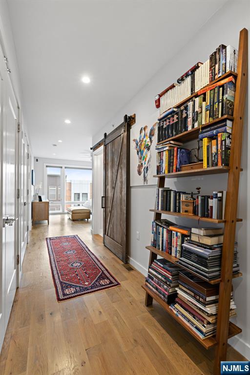 hallway with baseboards, a barn door, light wood-type flooring, and recessed lighting