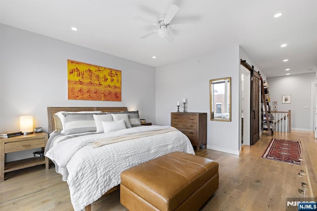 bedroom with light wood-style floors, recessed lighting, baseboards, and a barn door