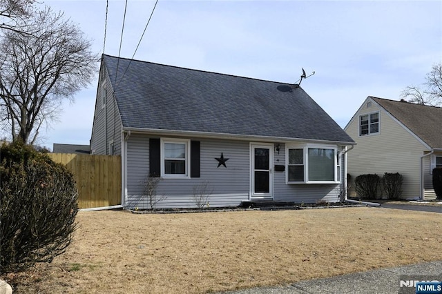 view of front of home with roof with shingles, fence, and a front lawn