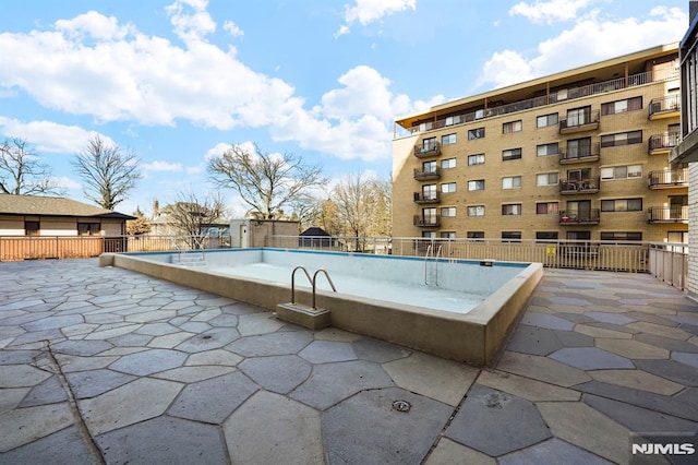 community pool with a patio area and fence