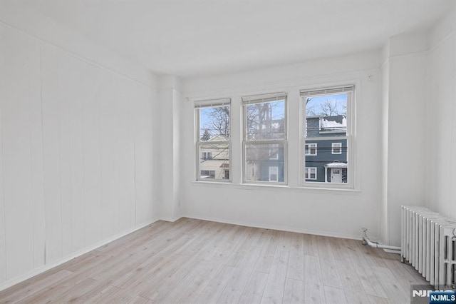 unfurnished room with light wood-style floors, radiator heating unit, and baseboards