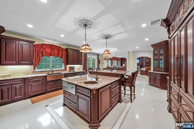 kitchen featuring arched walkways, a sink, visible vents, hanging light fixtures, and an island with sink