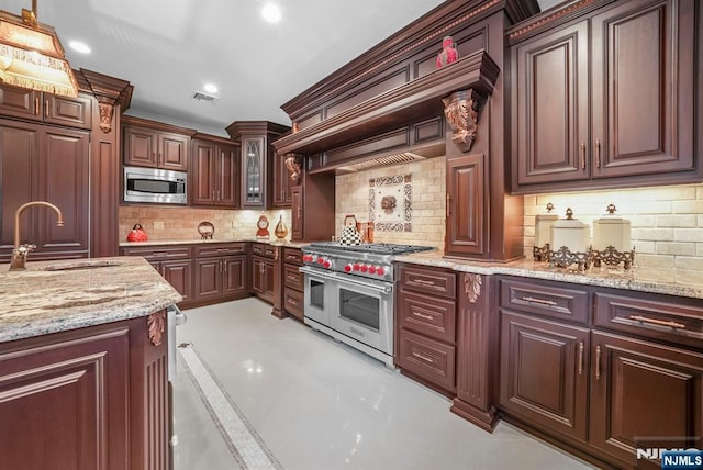 kitchen featuring light stone counters, decorative light fixtures, appliances with stainless steel finishes, glass insert cabinets, and a sink