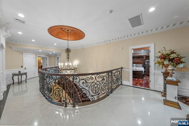 corridor with a wainscoted wall, visible vents, a decorative wall, and an inviting chandelier