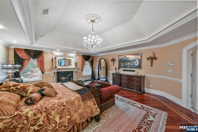 bedroom featuring visible vents, a raised ceiling, wood finished floors, crown molding, and a fireplace