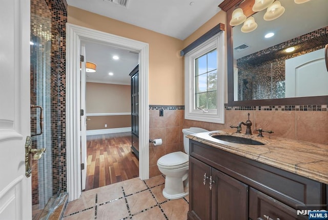 bathroom with a stall shower, visible vents, toilet, vanity, and tile walls