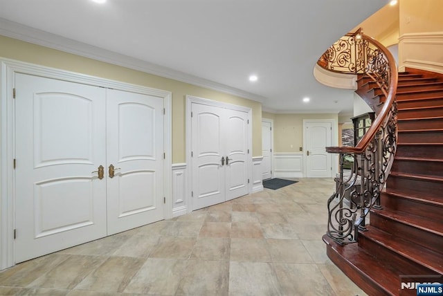 foyer featuring recessed lighting, a decorative wall, stairs, wainscoting, and crown molding