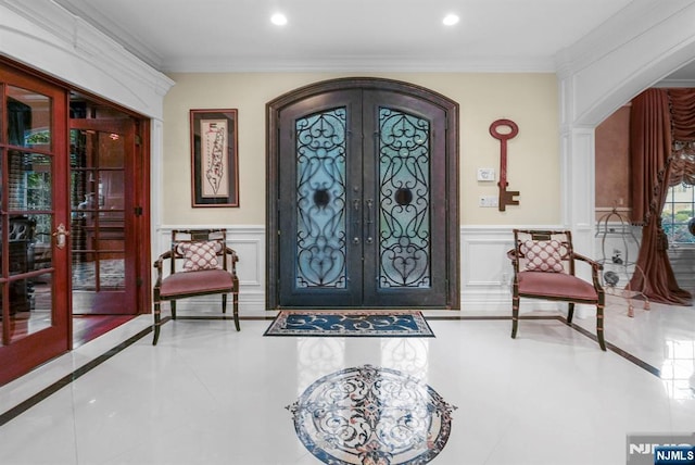 foyer featuring arched walkways, french doors, recessed lighting, a decorative wall, and ornamental molding