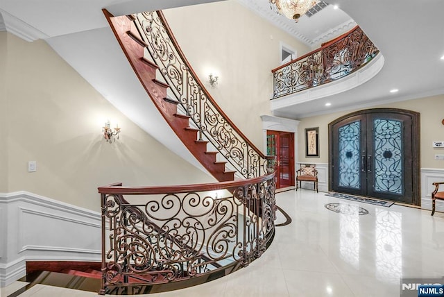 entryway with arched walkways, french doors, a wainscoted wall, a decorative wall, and ornamental molding