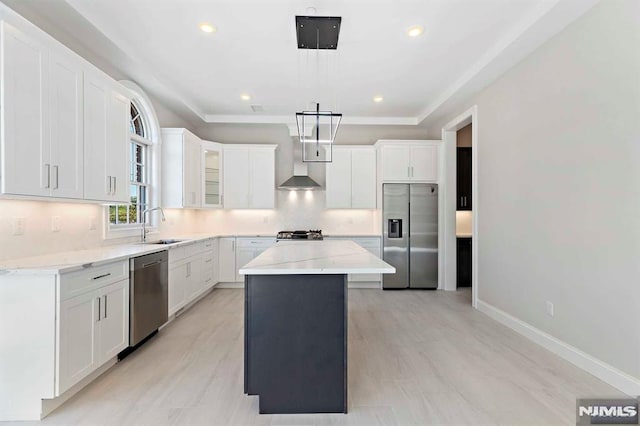 kitchen featuring white cabinets, hanging light fixtures, appliances with stainless steel finishes, a center island, and wall chimney exhaust hood