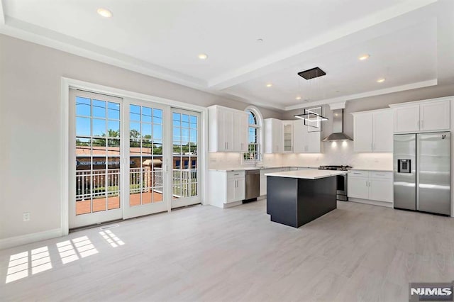 kitchen featuring a center island, pendant lighting, stainless steel appliances, light countertops, and wall chimney range hood