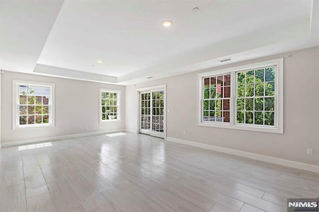 empty room with light wood finished floors, a raised ceiling, visible vents, and baseboards