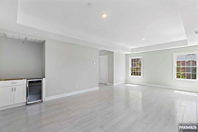 unfurnished living room with light wood finished floors, beverage cooler, baseboards, a raised ceiling, and recessed lighting