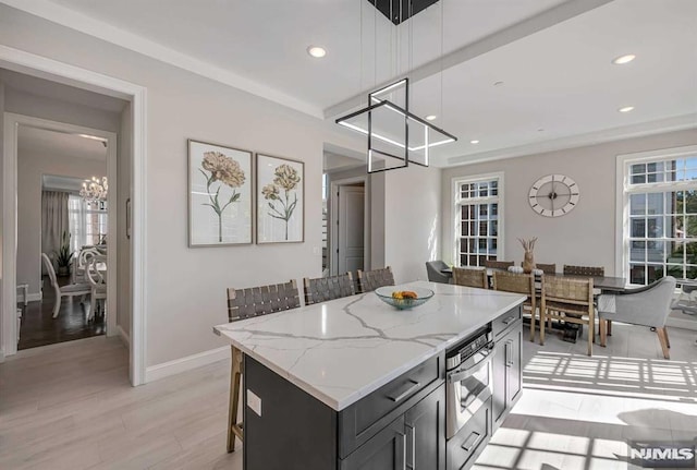 kitchen with a breakfast bar area, light stone counters, a center island, dark cabinetry, and pendant lighting