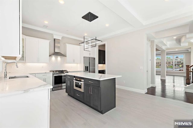 kitchen with wall chimney exhaust hood, a kitchen island, appliances with stainless steel finishes, pendant lighting, and a sink