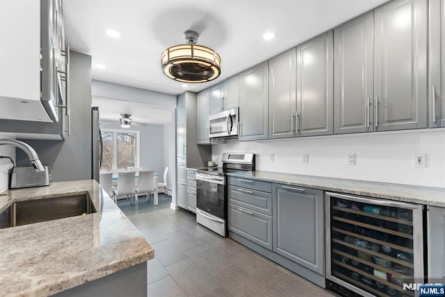 kitchen featuring stainless steel appliances, gray cabinetry, a sink, light stone countertops, and beverage cooler