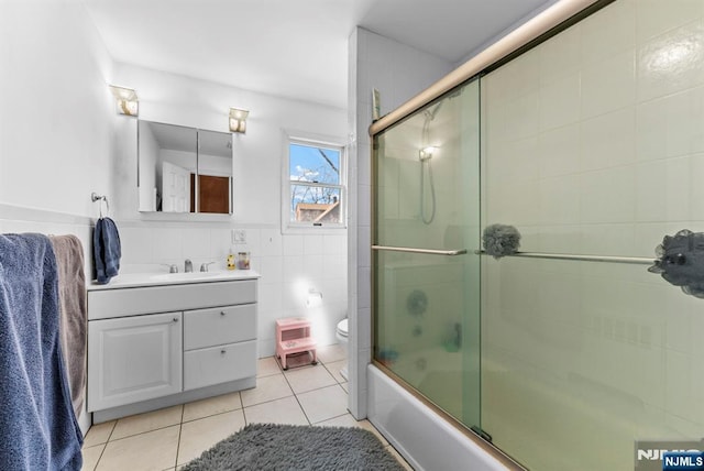 full bath featuring bath / shower combo with glass door, toilet, tile patterned floors, vanity, and tile walls