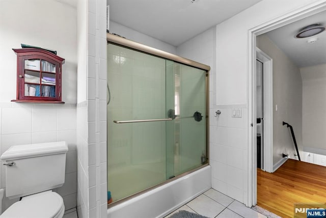 full bathroom featuring toilet, a wainscoted wall, tile patterned floors, combined bath / shower with glass door, and tile walls