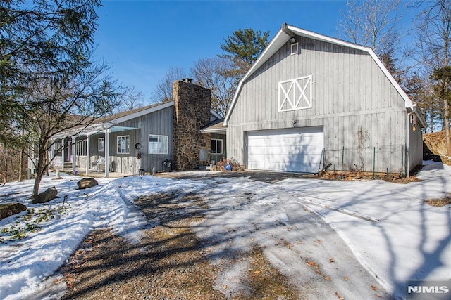 snow covered property featuring a barn, driveway, and a chimney