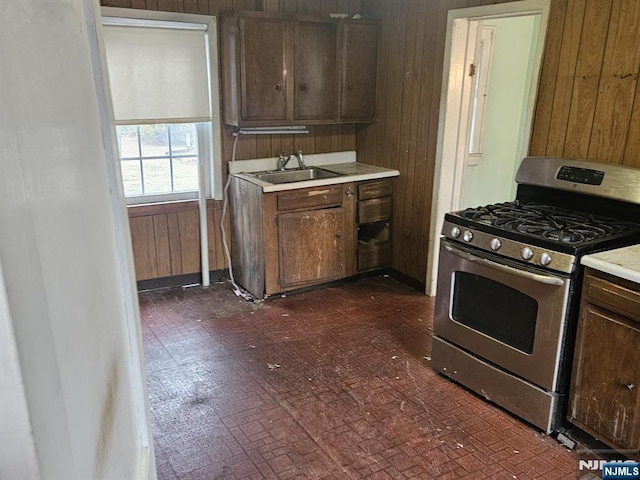 kitchen featuring light countertops, stainless steel gas stove, a sink, and wood walls