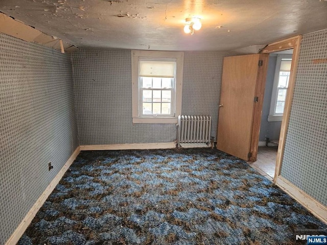 carpeted empty room with radiator heating unit and wallpapered walls