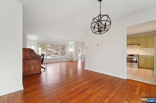 unfurnished living room with an inviting chandelier, baseboards, and light wood finished floors