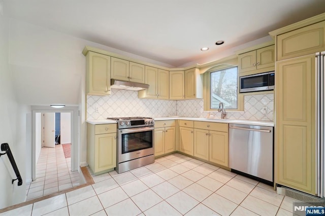 kitchen with decorative backsplash, appliances with stainless steel finishes, light countertops, under cabinet range hood, and a sink