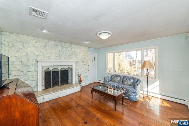 living room featuring a fireplace, visible vents, baseboard heating, and hardwood / wood-style floors