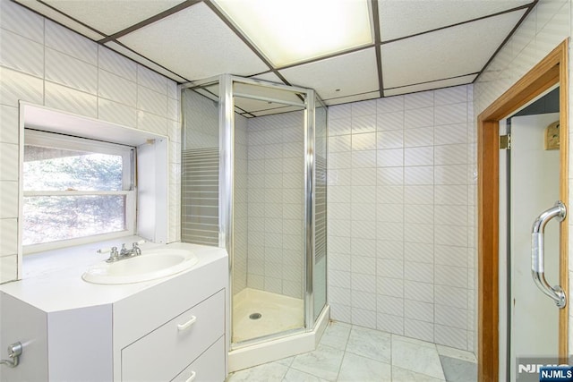 bathroom featuring tile walls, a paneled ceiling, a shower stall, and vanity