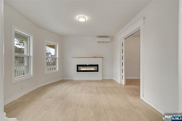 unfurnished living room featuring light wood finished floors, a wall mounted air conditioner, a glass covered fireplace, and baseboards