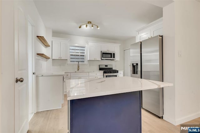 kitchen featuring appliances with stainless steel finishes, a kitchen island, white cabinetry, and light wood-style floors