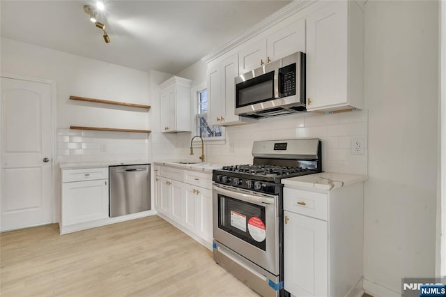 kitchen with white cabinets, appliances with stainless steel finishes, light wood-style floors, open shelves, and a sink