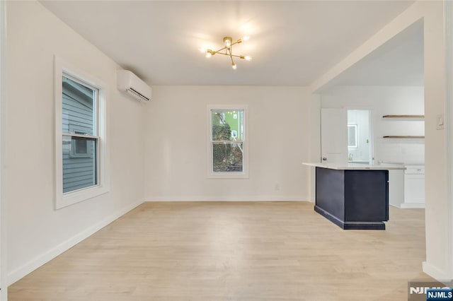 interior space featuring a wall unit AC, light wood-type flooring, baseboards, and a notable chandelier