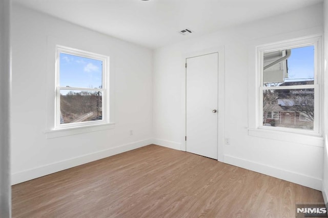 empty room featuring wood finished floors, visible vents, and baseboards