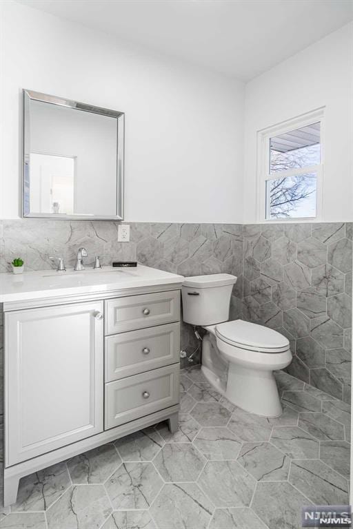 half bathroom featuring tile walls, a wainscoted wall, vanity, and toilet