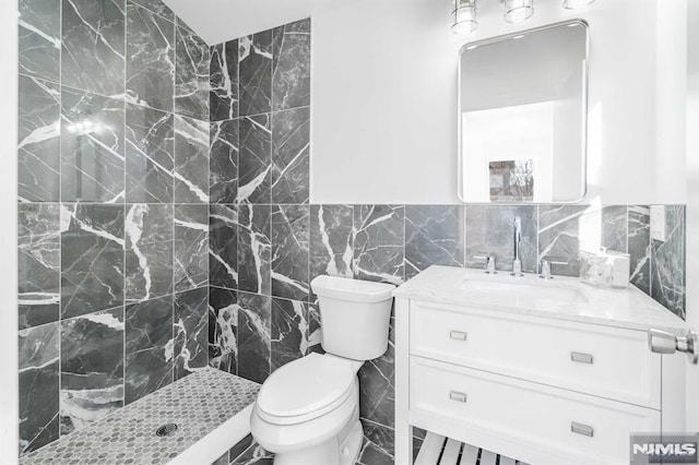 bathroom with toilet, vanity, tile walls, and tiled shower