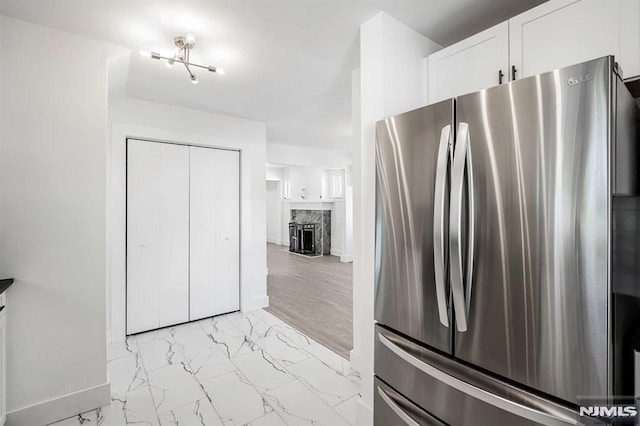 kitchen featuring marble finish floor, a fireplace, freestanding refrigerator, white cabinets, and baseboards