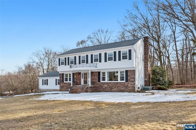 colonial inspired home featuring brick siding, a chimney, central AC, and a yard