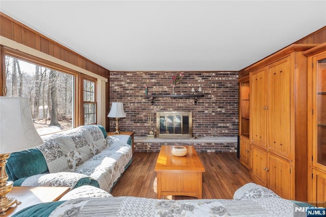 living area featuring a fireplace, wooden walls, brick wall, and hardwood / wood-style flooring