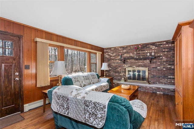 living room with hardwood / wood-style flooring, brick wall, wood walls, a fireplace, and a baseboard heating unit