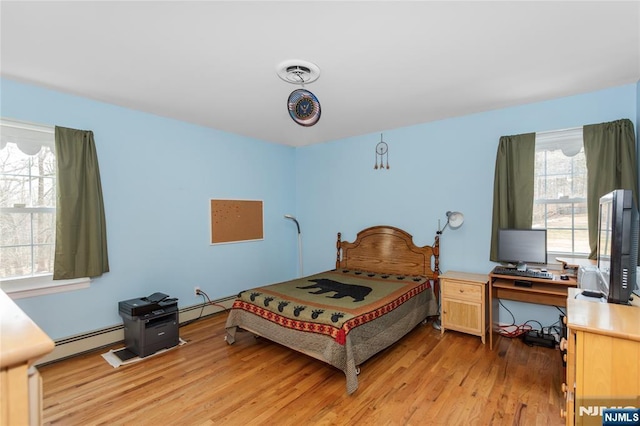 bedroom with a baseboard heating unit, light wood-style flooring, and visible vents