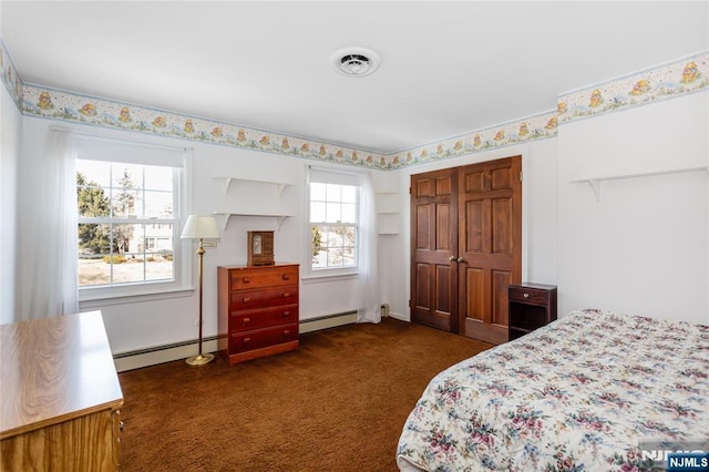 bedroom with a baseboard heating unit, visible vents, and dark carpet